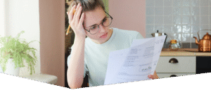 Indoor shot of young European Caucasian girl looking at financial documents at home with deeply bored face looking sick and tired of her economic problems, trying to check counts and all details