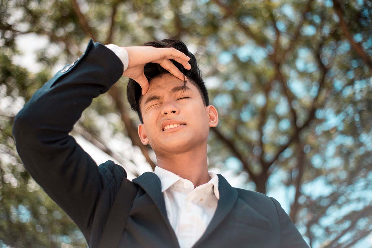 A young absentminded asian university student clenches his foreh